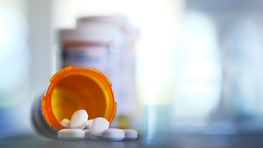 Pills spilling out of open pill bottle on table.